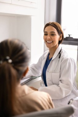 Laboratuvar önlüklü neşeli genç doktor klinikteki iş yerinde hastayla görüşüyor, konsültasyon yapıyor, kadınlarla konuşuyor, gülümsüyor, gülüyor, sağlık hizmetleri hakkında iyi haberler veriyor. Dikey çekim