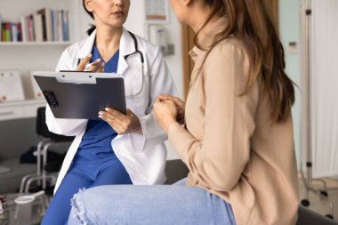 Muayeneden sonra genç hasta kadına danışan ciddi bir kadın doktor. Elinde kağıt kayıtlarla bir pano tutuyor. Kadınlarla konuşuyor, tıbbi kanepede oturuyor. Kırpılmış atış