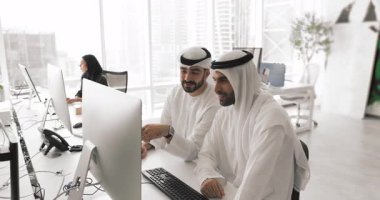 Yeni iş platformunu inceleyen iki Arap erkek meslektaşı, yatırım olanakları veya çağdaş çalışma ofisindeki bilgisayarla masada oturan proje güncellemeleri. İşbirliği, modern teknoloji