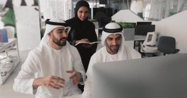 Geleneksel kandura ve tesettüre bürünmüş üç Arap takım arkadaşı modern bilgisayar kullanarak görev tartışır, çevrimiçi proje üzerinde işbirliği yapar, güncelleme veya sunum gözden geçirir