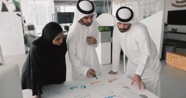 Üç Arap profesyonel erkek ve kadın kağıt pazarlama finansal raporlarıyla masada konuşuyor, yatırım stratejisini tartışıyor, karı, geliri ve araştırma sonuçlarını birlikte analiz ediyorlar.