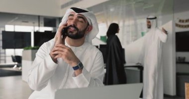 İş yerindeki iş arkadaşlarıyla cep telefonundan konuşan genç ve yakışıklı bir Arap işadamı. Arka planda çalışıyor, sohbetin keyfini çıkarıyor, iletişim kuruyor, gülümsüyor, telefonu kapatıyor.
