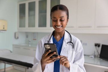 Mola sırasında akıllı telefon kullanan Afrikalı kadın doktor klinikte duruyor, e-sağlık uygulaması aracılığıyla hastaya danışıyor, hastane platformuna erişiyor, uzaktan iletişim kurmaktan tatmin oluyor.
