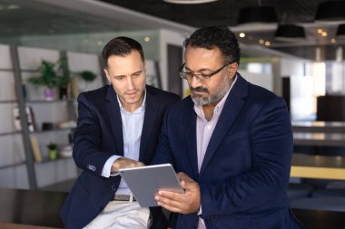 Olgun İspanyol adam eski meslektaşına tablette yeni şirket platformunu gösteriyor, yeni online görevi açıklıyor, modern aygıt ekranına birlikte bakıyor, sunumu gözden geçiriyor ya da toplantı için slaytları hazırlıyor