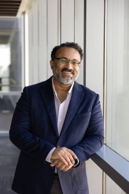 Modern ofis koridorunda pencerenin önünde duran resmi ceketli gülümseyen orta yaşlı Hintli işadamının portresi kurumsal başarıdan ve iş hayatında yeni fırsatlardan memnun. Profesyonellik
