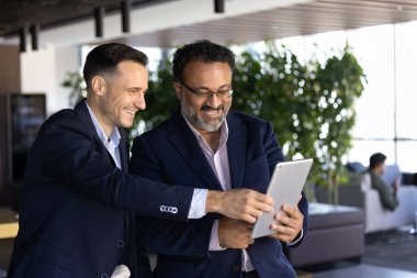 İki çoklu etnik çeşitlilikte gülümseyen takım arkadaşı tablet, sunum veya proje planı, strateji veya fikirler üzerinde işbirliği, verileri kontrol etme, ofiste üretken modern işbirliğinin tadını çıkarma,