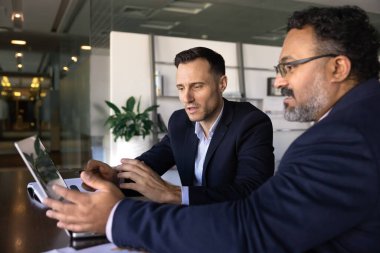 Modern ofiste dizüstü bilgisayarda birlikte çalışan iki odaklı işadamı mali raporları tartışıyor, pazar eğilimlerini analiz ediyor, işlerini büyütmek ve proje sonuçlarını iyileştirmek için stratejik kararlar alıyorlar.