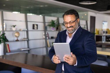 İş adamı tablete neşeli bir ifadeyle bakıyor, meslektaşlarına veya müşterilerine video çağrısı yapıyor, başarılı proje dönüm noktasını tartışıyor veya üretken uzaktan iletişimle meşgul olan olumlu haber alışverişinde bulunuyor