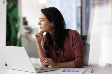 Düşünceli bir şekilde masasına oturmuş, düşünceli bir ifadeyle, düşünceli bir ifadeyle, beyin fırtınası yaparak, plan yaparak ya da modern iş yerinde stratejik kararları düşünerek dikkati dağılmış bir kadın.