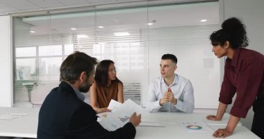 Olumlu çok ırklı iş arkadaşları, hissedarlar, yatırımcılar, iş ortakları toplantı masasında beyin fırtınası yaparak ürün pazarlama araştırma sonuçları, iş stratejisi, yatırım konularını tartışıyorlar.