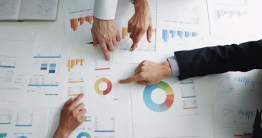Kağıt pazarlama raporlarındaki çizelgelere işaret eden iş arkadaşlarının elleri, ürün satışlarının büyümesini analiz eden, analitik veriler, iş projesi stratejisini tartışan. Diyagramların üst görünümü, kırpılmış çekim