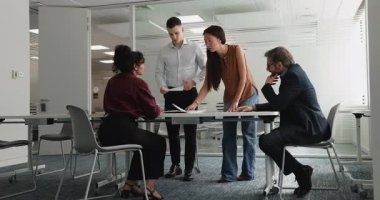 İki proje yöneticisi patronlara, yatırımcılara satış raporlarını sunuyor toplantı masasındaki iş arkadaşlarına kağıt belgeler veriyorlar. İş arkadaşları pazarlama araştırma sonuçlarını tartışıyor