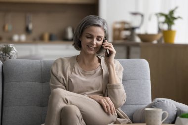 Neşeli, güzel, gri saçlı bir kadın cep telefonuyla konuşuyor, sohbetin tadını çıkarıyor, kablosuz bağlantının tadını çıkarıyor, olumlu telefon konuşmalarının tadını çıkarıyor, gülümsüyor, gülüyor.