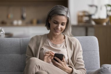 Neşeli, olgun bir kadın akıllı telefonuyla internet üzerinden iletişim kuruyor, daktilo çekiyor, kanepede dinleniyor, internette boş vakitlerin tadını çıkarıyor, gülümsüyor, gülüyor.