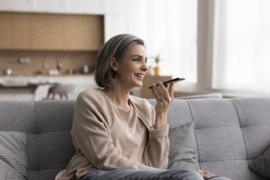 Neşeli, rüya gibi olgun bir kadın, hoparlörden arıyor, akıllı telefonu yüzüne tutuyor, konuşuyor, sesli mesaj kaydediyor, gülümsüyor, gülüyor, eğleniyor, evde iletişim kuruyor.