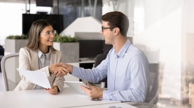 Birkaç mutlu genç Latin iş ortağı ofis masasında el sıkışıyor, anlaşma sağlıyor, kağıt belgeler ve dijital tablet bilgisayarı tutuyor, gülümsüyor, tokalaşmayı bitiriyor.