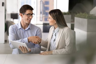 İki pozitif şirket çalışanı iş yerinde el sıkışıyor. Genç Latin işadamı ofis masasındaki profesyonel danışmana el sıkışırken elinde tablet bilgisayarla gülümsüyor.