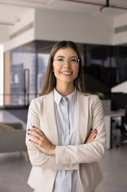 Ofiste kolları kavuşturulmuş, yalnız başına kameraya gülümseyen neşeli, kendine güvenen profesyonel bir iş kadını. Mutlu güzel finansal ya da hukuki uzman, kadın lider dikey portresi