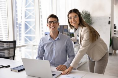 Bir çift mutlu genç iş adamı dizüstü bilgisayarda oturmuş, iş yerinde personel portresi için poz veriyorlar. Gözlüklü iki pozitif iş arkadaşı, başarılı şirket yöneticileri portresi.