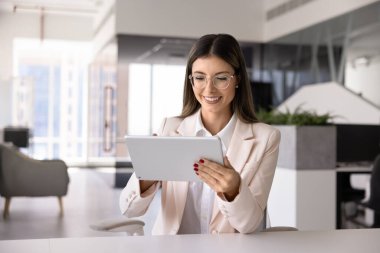 Mutlu genç İspanyol iş kadını modern internet teknolojisini etkin çalışma süreci için kullanıyor, iş yerinde tablet yazıyor, çevrimiçi içeriği izliyor, satışları izliyor