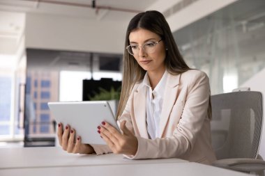 Zarif gözlüklü, ciddi bir İspanyol yönetici kadın. Tabletten online iş videosu izliyor, iş yerindeki dijital dokunmatik bilgisayarını kullanıyor, internette geziniyor.