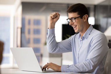 Neşeli duygusal İspanyol menajer iş başarısını kutluyor, yumruk zaferi kazanıyor evet el hareketi dizüstü bilgisayarda, e-posta alıyor, iyi haberlerle çevrimiçi mesaj alıyor, gülümsüyor, gülüyor.