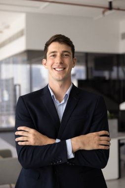 Ofiste poz veren başarılı genç İspanyol iş adamı ellerini çapraz yapıp kameraya bakıyor ve gülümsüyor. Pozitif, genç, hırslı çalışan portresi.