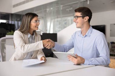 Pozitif genç İspanyol iş ortakları mali satış raporlarını tartıştıktan sonra anlaşmayı kapatıyorlar, tablet ve kağıt belgelerini tutuyorlar, toplantı masasında el sıkışıyorlar, gülümsüyorlar.