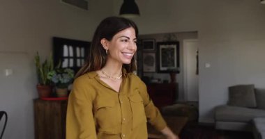 Happy young 30s Hispanic woman dancing at new home, moving body, having fun, laughing, enjoying favorite music, songs, party, active leisure in living room, celebrating good news