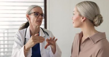Senior female doctor in glasses giving consultation, medical advice to young patient, talking to woman in clinic office, explaining examination result, diagnosis, treatment recommendation
