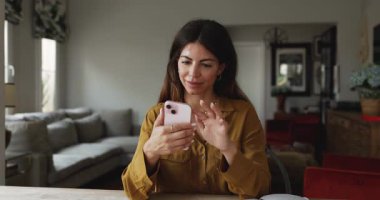 Positive Latin freelancer woman typing on mobile phone, using online business app on gadget for remote work communication, sitting at home office table, texting email, message,