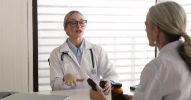 Young GP doctor woman prescribing medications to patient, giving glass bottles with pills, syrup, telling about vitamins, drugs, giving recommendation, medical advice for therapy