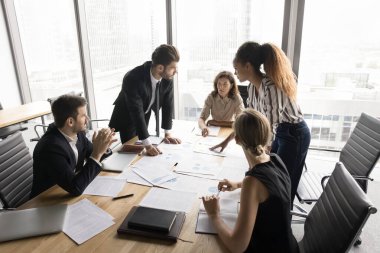 İş ekibi çalışması. Çeşitli etnik kökenlere sahip profesyonel yöneticilerden oluşan modern ekip, işbirlikçi proje inceleme belgeleri üzerinde beyin fırtınası atölyesinde çalışarak kriterleme için istatistiksel verileri tartıştılar.