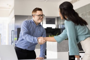 Genç İspanyol iş kadını, iş arkadaşı, profesyonel, Down sendromlu bir danışman ile el sıkışıyor, iş yeri masasında el sıkışıyor ve işbirliği için teşekkür ediyor.