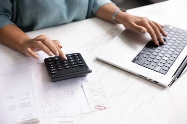 Ofis masasında dizüstü bilgisayar ve hesap makinesi kullanan, şirket bütçesini planlayan, gelir hesaplayan, masrafları hesaplayan, kağıt faturalarını yazan profesyonel bir kadın. Kırpılmış kollar