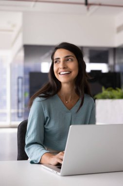 Ofiste dizüstü bilgisayarda yazan, online ürün üzerinde çalışan, blog için makale yazan, başka yöne bakan, yaratıcı fikirler düşünen mutlu, başarılı genç İspanyol iş kadını. Dikey çekim