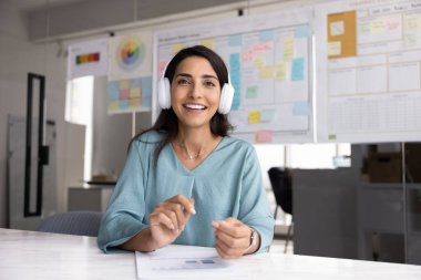 Neşeli, güzel, Latin proje yöneticisi, kulaklık takan bir kadın çevrimiçi video konferans görüşmesinde konuşuyor, kameraya bakıyor ve dişlek gülümsemesiyle konuşuyor. Ekran başı resmi