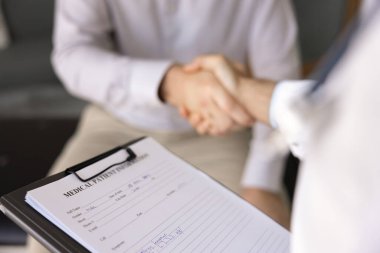 Paltolu ve hastane çalışanı ile hastanın el sıkışırken ki görüntüsünü kapat. Hasta bilgilerine odaklan. Sağlık hizmetleri, sağlık sigortası ve profesyonel bakım