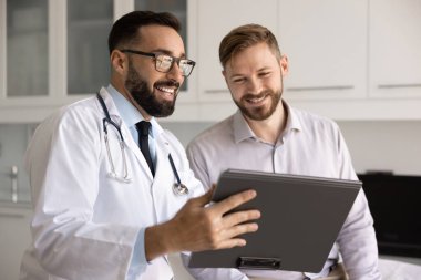 Hasta muayenehanesinde dijital tablet kullanan doktor, bilgiye erişmek veya teletıp araçlarını açıklamak, sigorta detaylarını gözden geçirmek, sağlık tavsiyelerini veya prosedür listesini paylaşmak