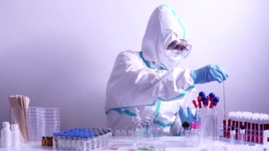 Ekipmanlı tıbbi laboratuvar ve Pediatri önlüğü giyen mikrobiyoloji uzmanı, yüz koruyucu maske takan cam kaplar, çeşitli doku ve kan örnekleriyle çalışıyor. Aşı geliştirmek, uyuşturucu araştırması.
