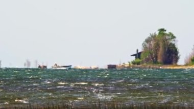 Long distance and very hot summer air make jelly effect at lake water and fishermen on the boat. Cottage life on the lake depiction, relaxing tranquil fishing on a boat at peaceful summer.