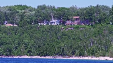 Cottages at limestone rocky cliff with green forest by Lake Huron Lion's Head Beach Harbour in Lion's Head Provincial Park Ontario Canada. Isthmus Bay, Lion's Head Point. Houses for seasonal vacation
