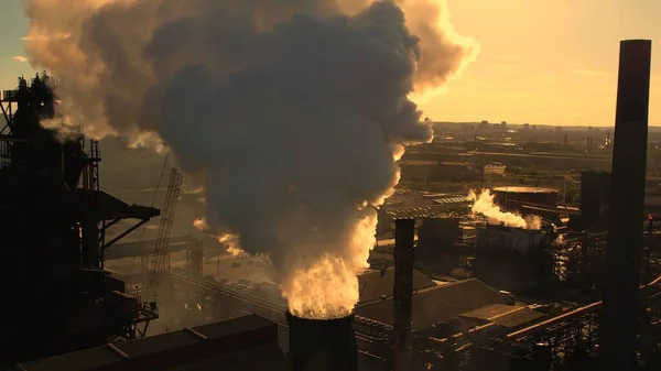 日没の時間と黄金の時間の間に鋼管 濃い煙の後ろに日光 冶金工場と煙雲は煙突から来ている温室効果ガスゾーン層を作成します 気候変動 — ストック写真