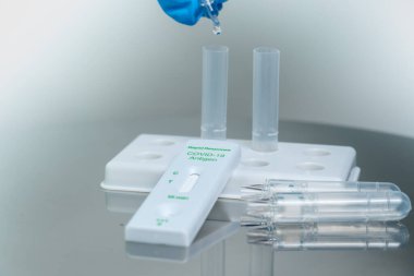 Close up of male nurse in blue gloves drops test reagents to extraction buffer tubes. Qualitative detection of Covid 19 vital antigens in nasal swab specimens. For self testing.  clipart