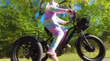 Traveler woman in silly unicorn pyjama dress riding on electric bike, E-bike or bicycles at sunny day in the forest park. Summertime lightning. Active tourism, rides in North America park.
