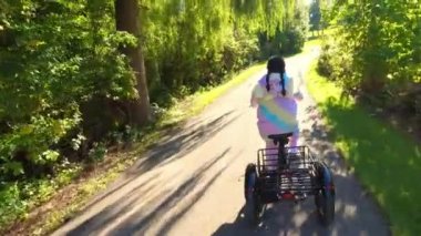 Woman in funny and crazy colourful unicorn dress riding an electric bicycle and smiling happy at sunny day. Cheerful happy woman having fun while on the e bike at green park trail. Ecology concept.
