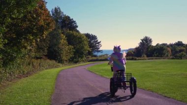 Traveler woman in silly unicorn pyjama dress riding on electric bike, E-bike or bicycles at sunny day in the forest park. Summertime lightning. Active tourism, rides in North America park.