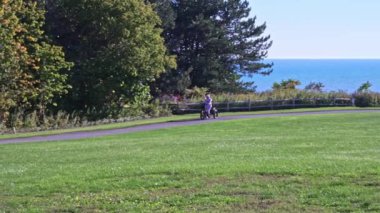 Women dressed as cartoon character unicorn on electric bicycle riding in the green sunny park. Rainbow colour silly pyjama costume. Humour and funny silly activity on the bike.