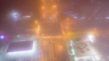 City main intersection at thick foggy night. Cinematic diffusion effect at cars transportation junction activity. Expressway view from above with night lights and illumination.