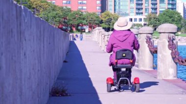 Woman who has disability in the wheelchair mobility scooter enjoying summer park near lake water. Carefree woman with mobility issue uses electric three wheel wheelchair scooter having fun.